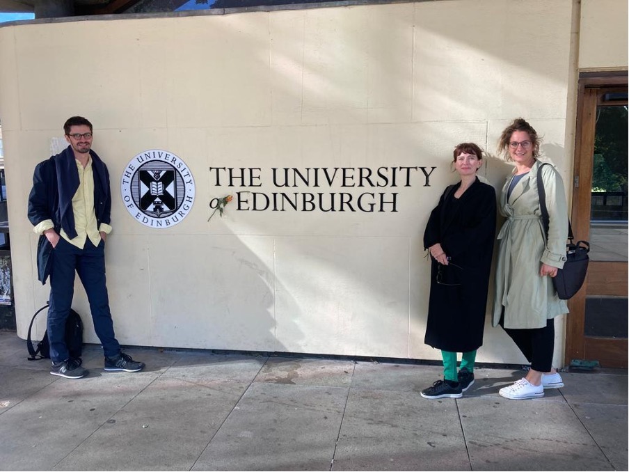 picture of two current and one former HUB member in front of the University of Edinburgh logo on a study trip to Scotland